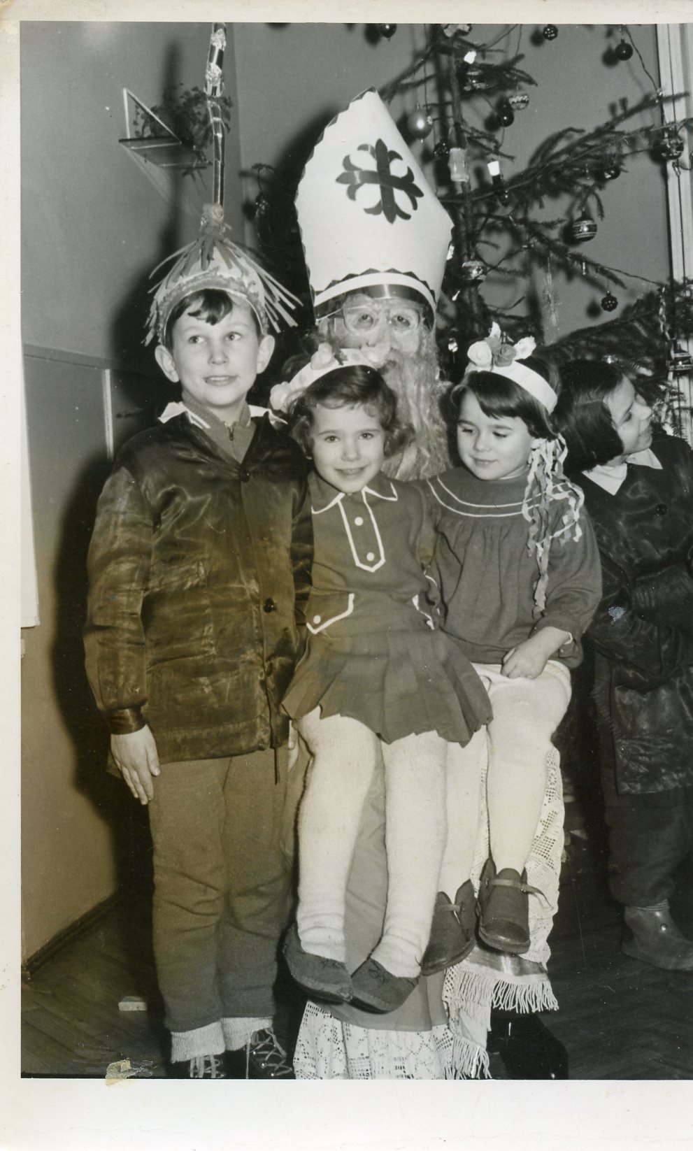 czarno biała fotografia przedstawiająca po lewej chłopca, dwie dziewczynki na kolanach Mikołaja i jedna stojąca po prawej a w tle choinka