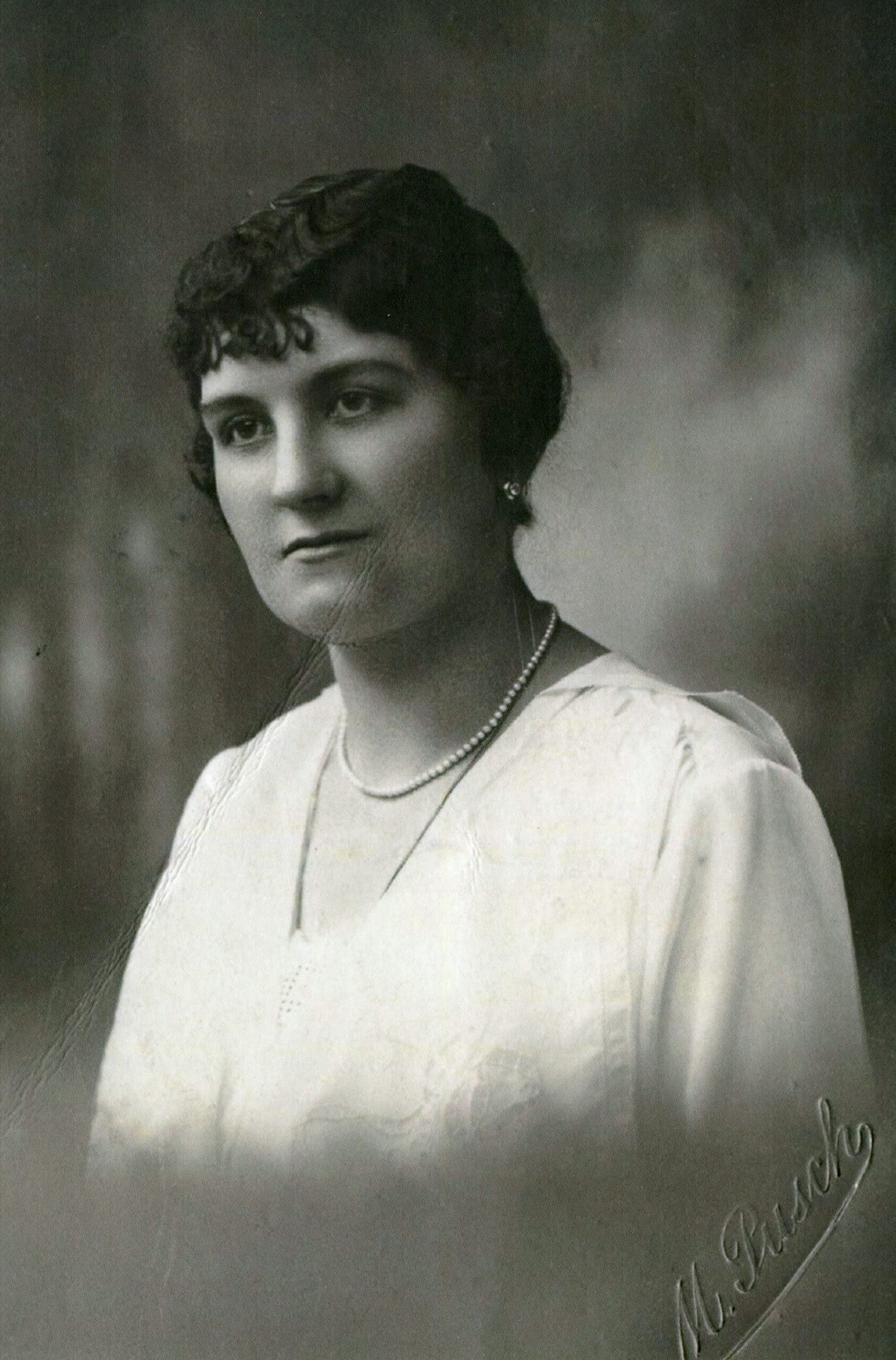 Portret kobiety z białej bluzce i z ciemnymi włosami.