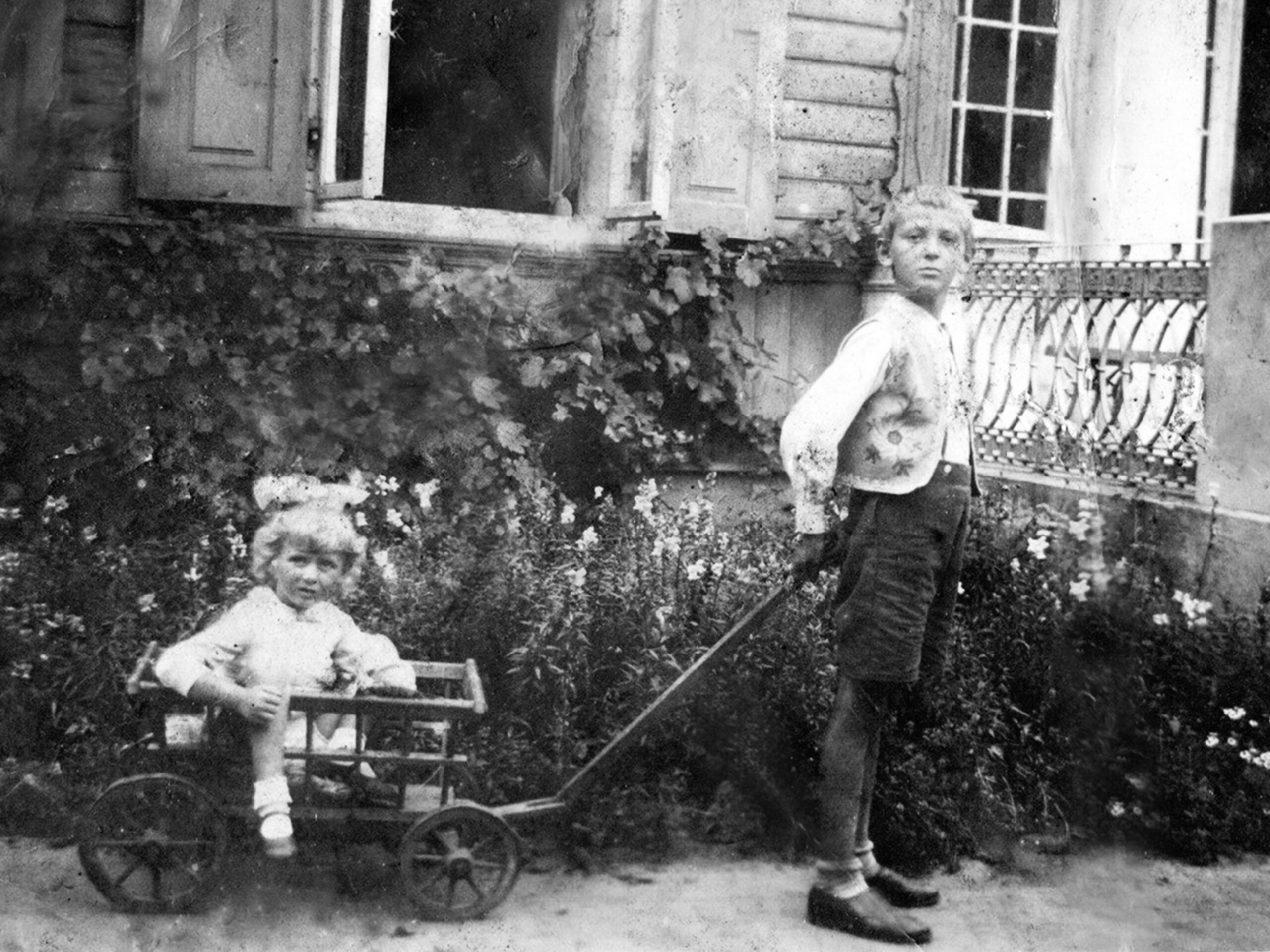 Na fotografii dwójka dzieci, chłopiec ciągnie w wózki dziewczynkę